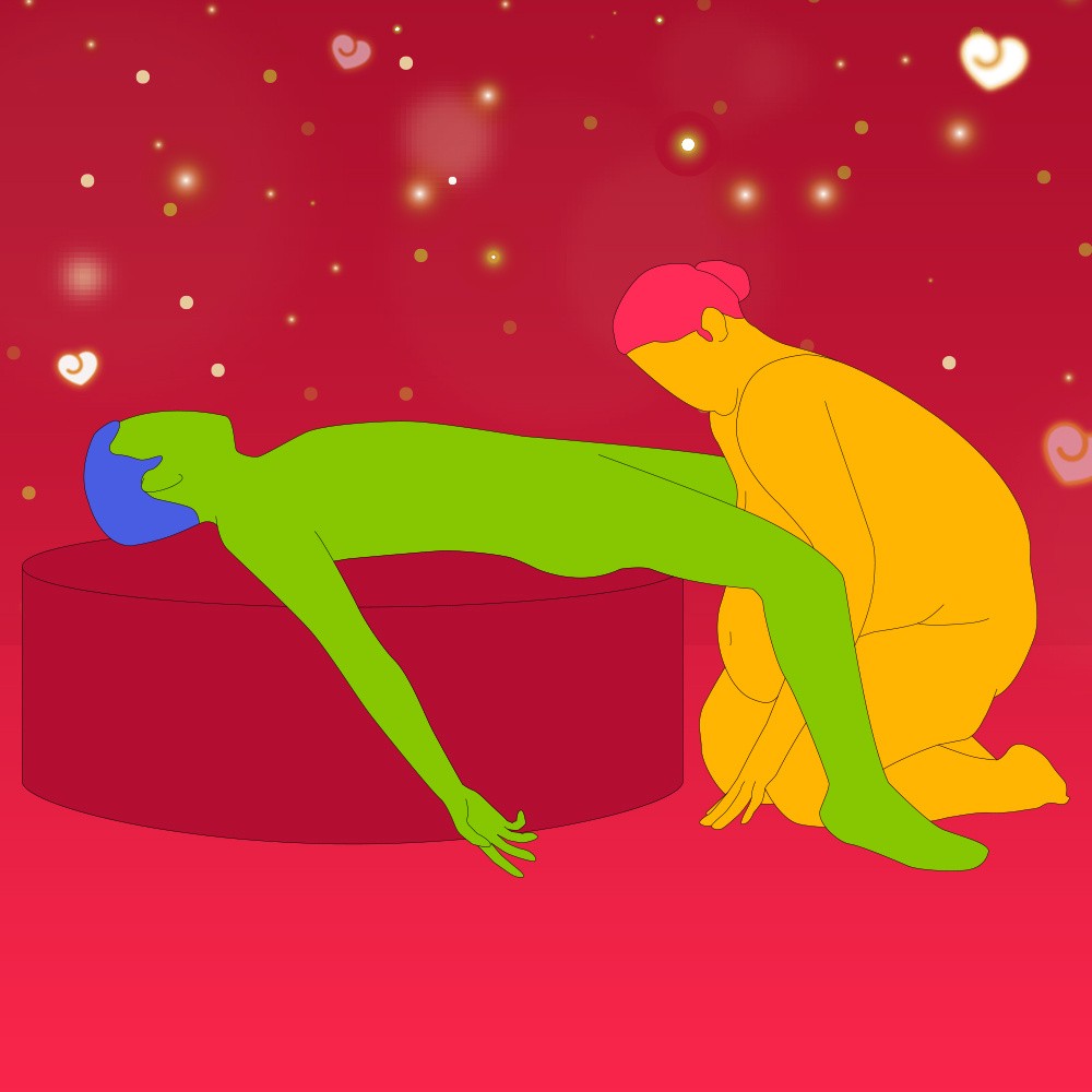 A naked illustrated couple in a seated position. One is led on their back on an ottoman and the other is crouched on their knees by their legs.